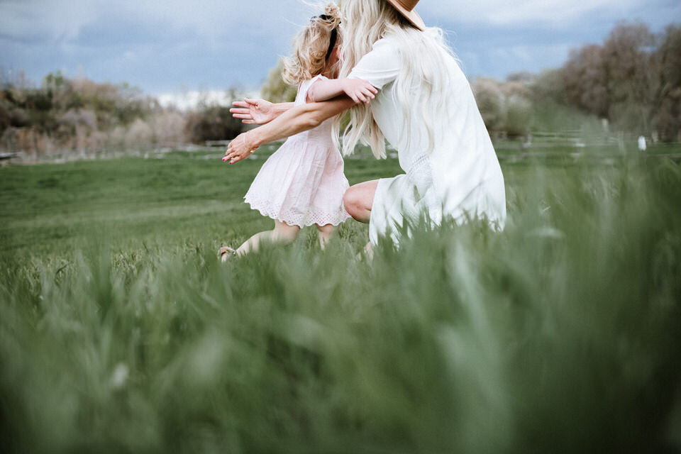 toddler girl running into her mom's arms for a hug in the grass