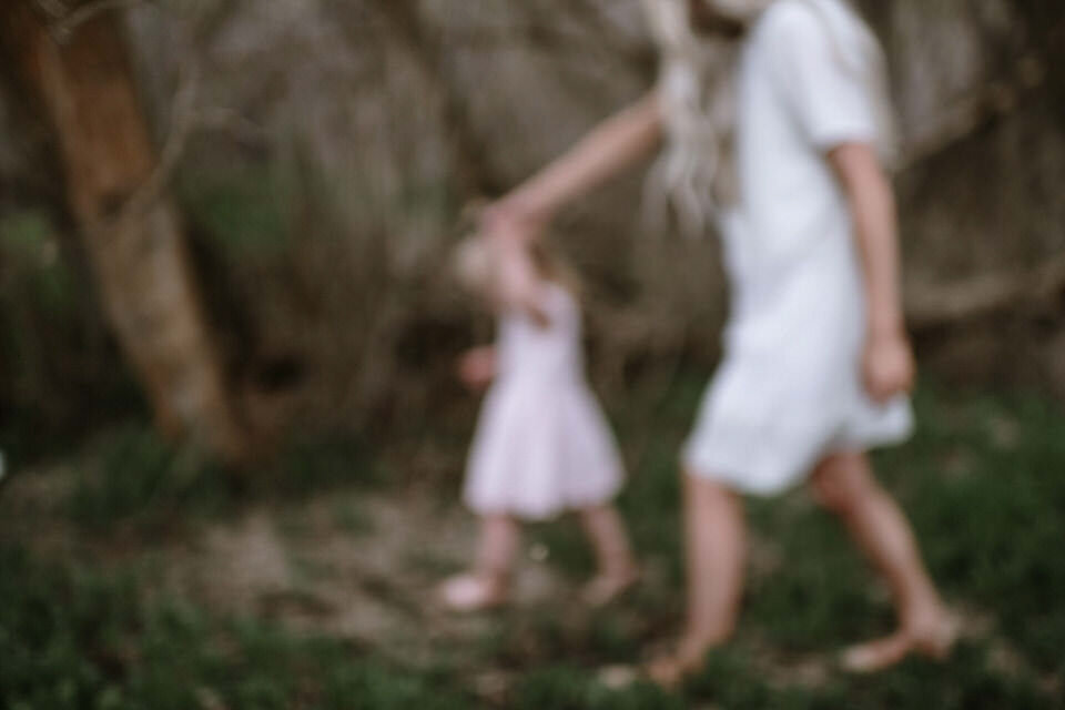 blurry photo of mom with long hair walking and holding daughter's hand