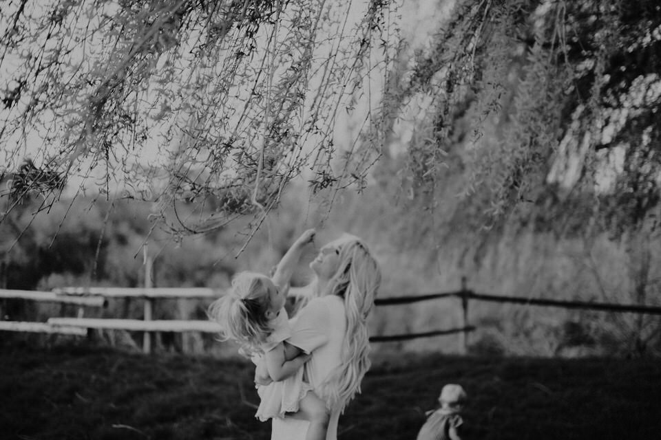 black and white photo of mom with toddler and baby under weeping willow tree