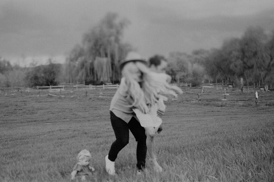 black and white film photo of dad picking up mom running in grassy field