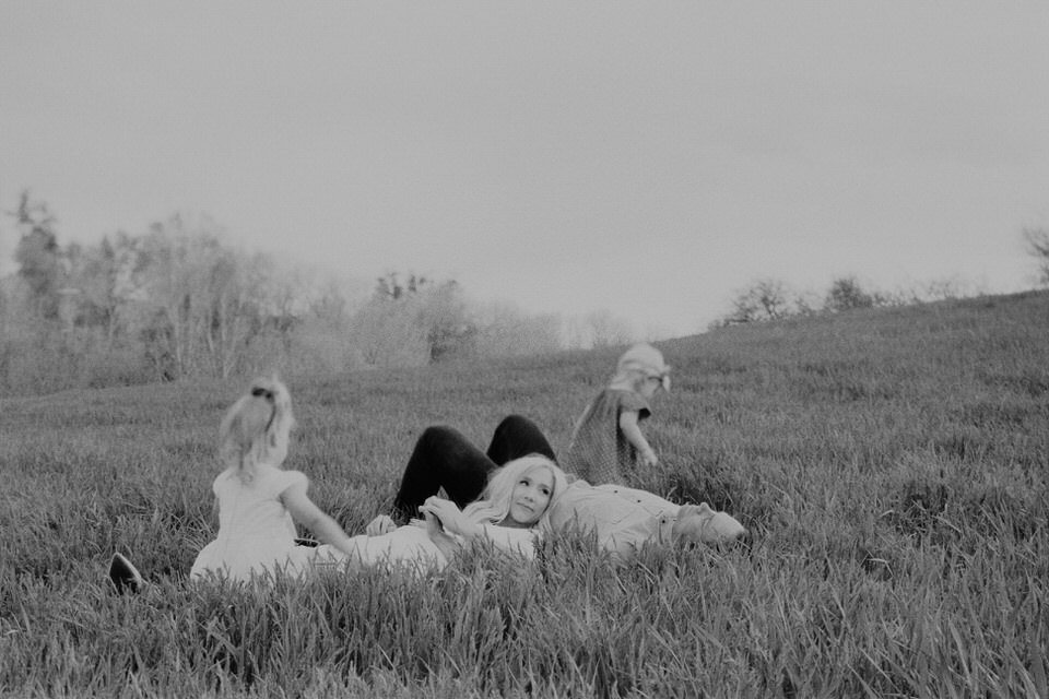 black and white film photo of family lying in grass in each others laps