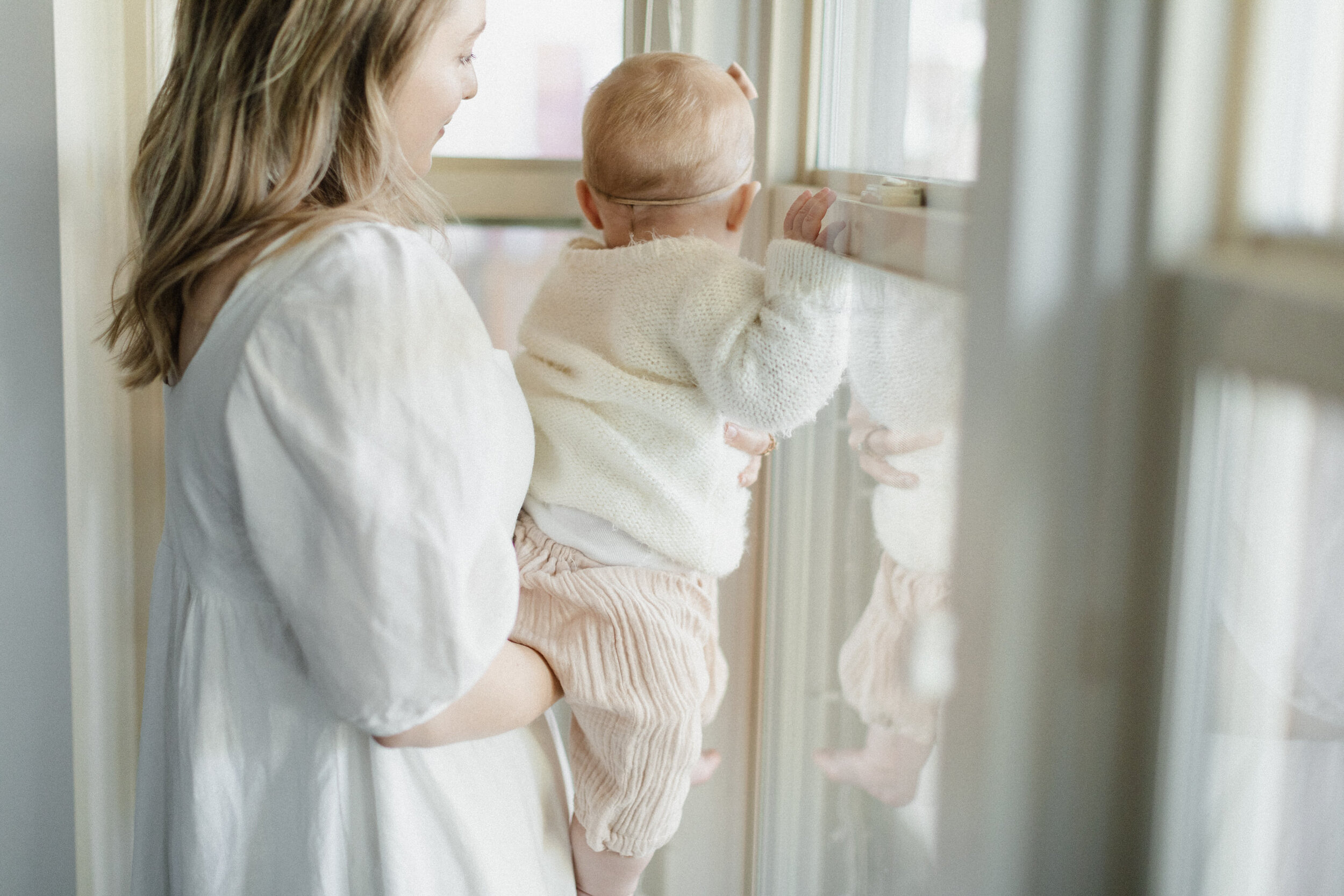 mom holding baby looking out windows