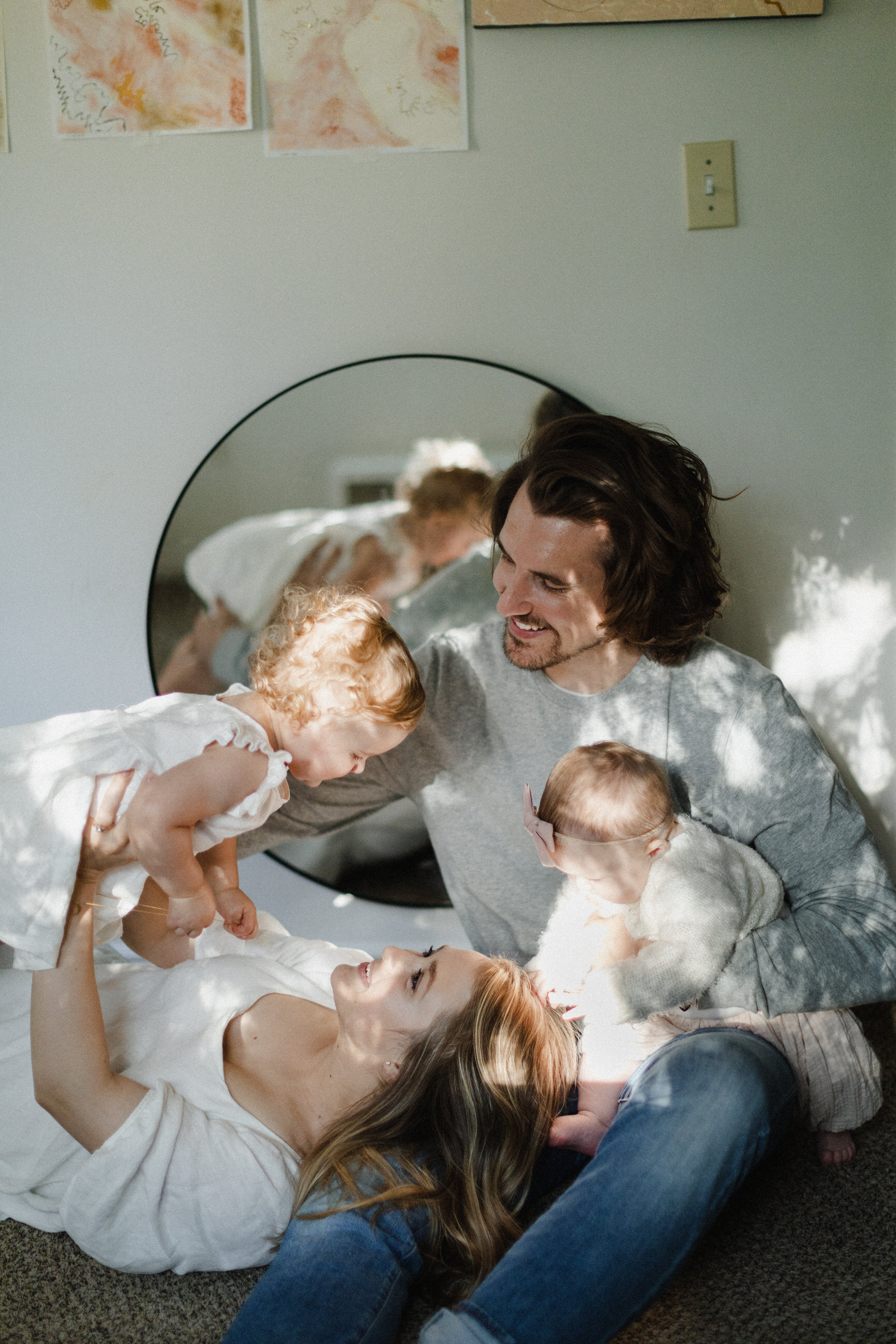 family sitting on floor holding babies with round mirror background