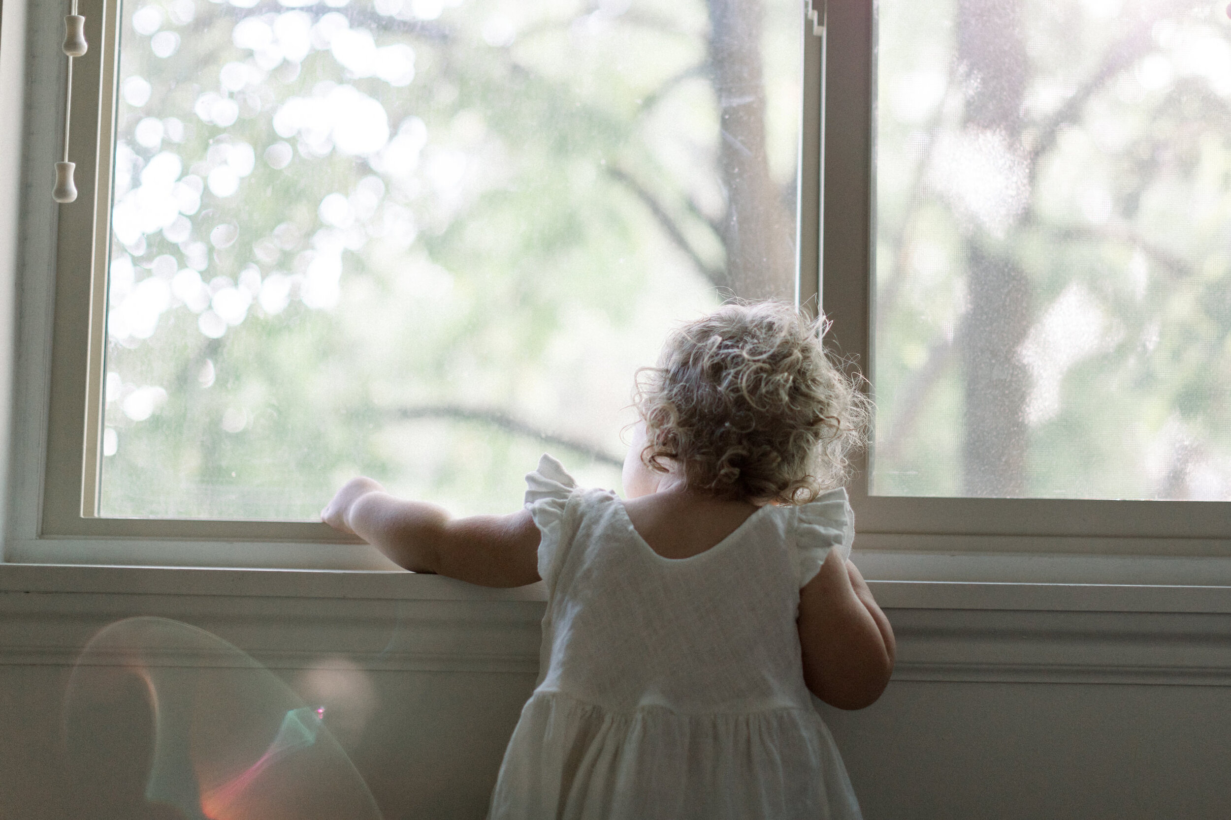 toddler looking out window with sun flare shining through