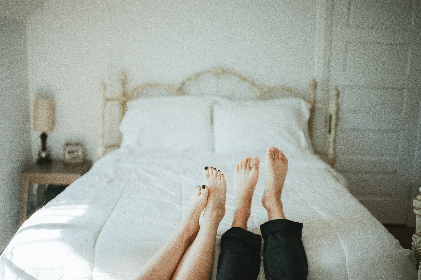 couple's feet propped up on bed with white sheets