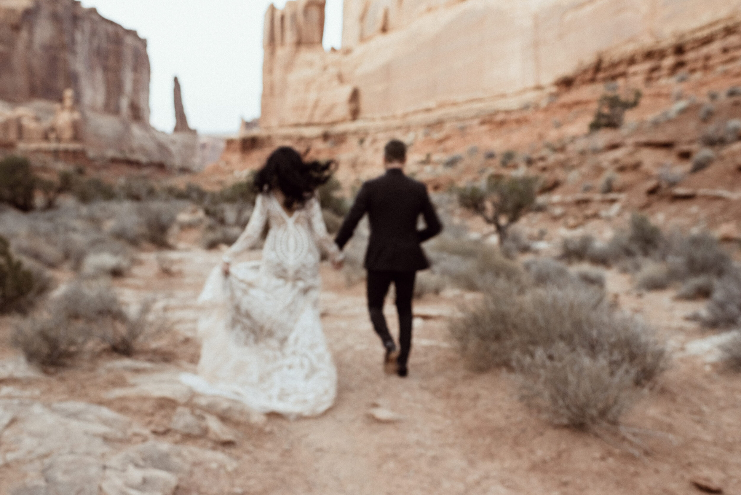 wedding couple running in desert with sandstone cliffs