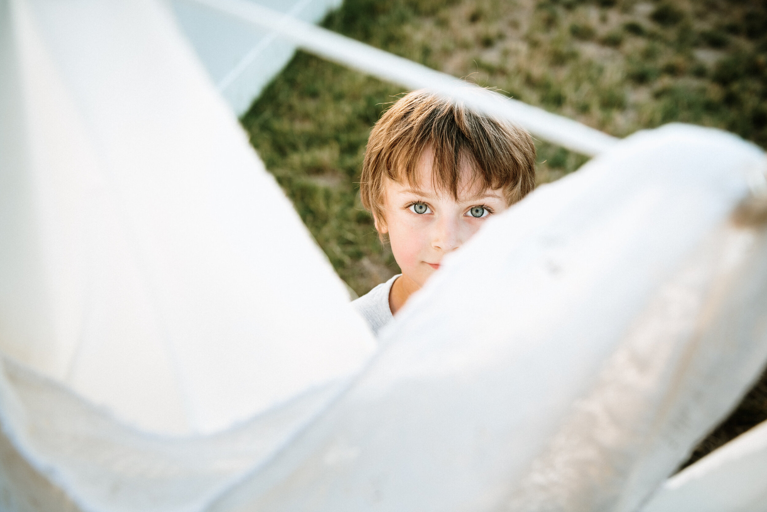 little boy looking up through white sheets in back yard