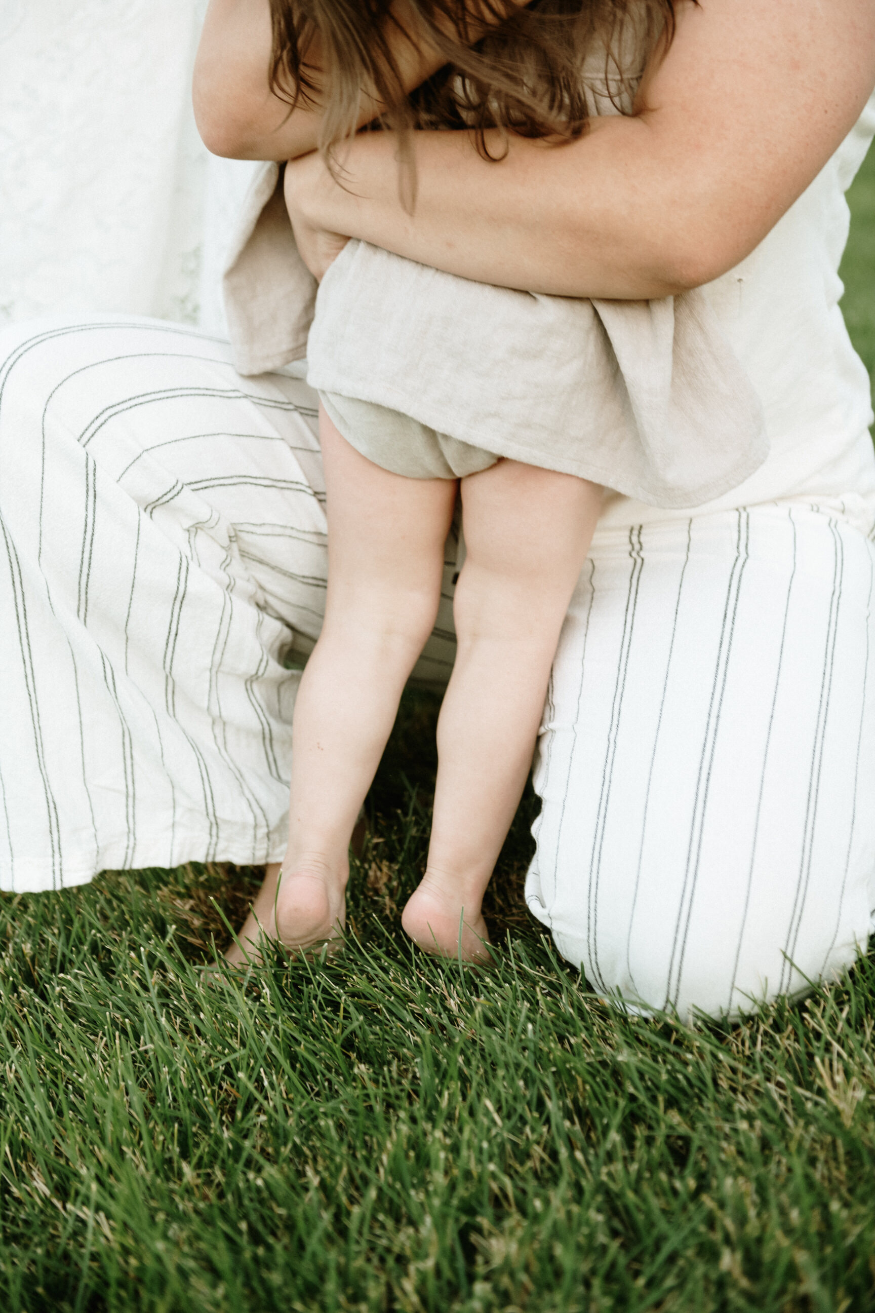 mom hugging toddler girl in grass