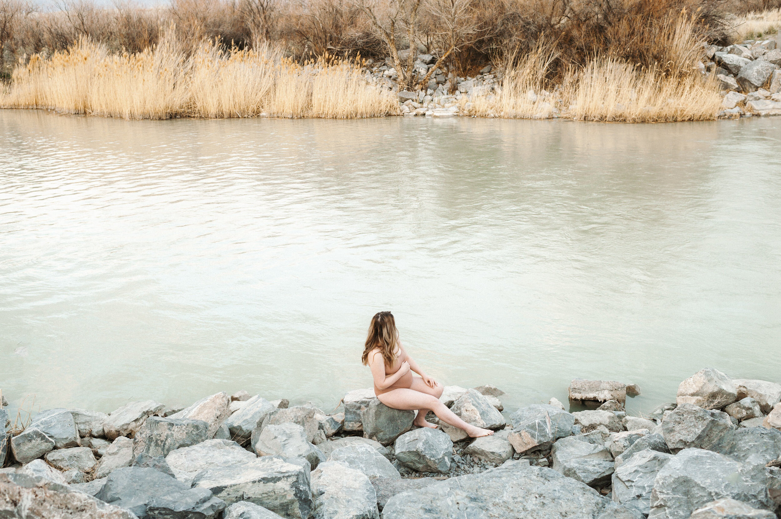 pregnant mom sitting on rocks in front of river