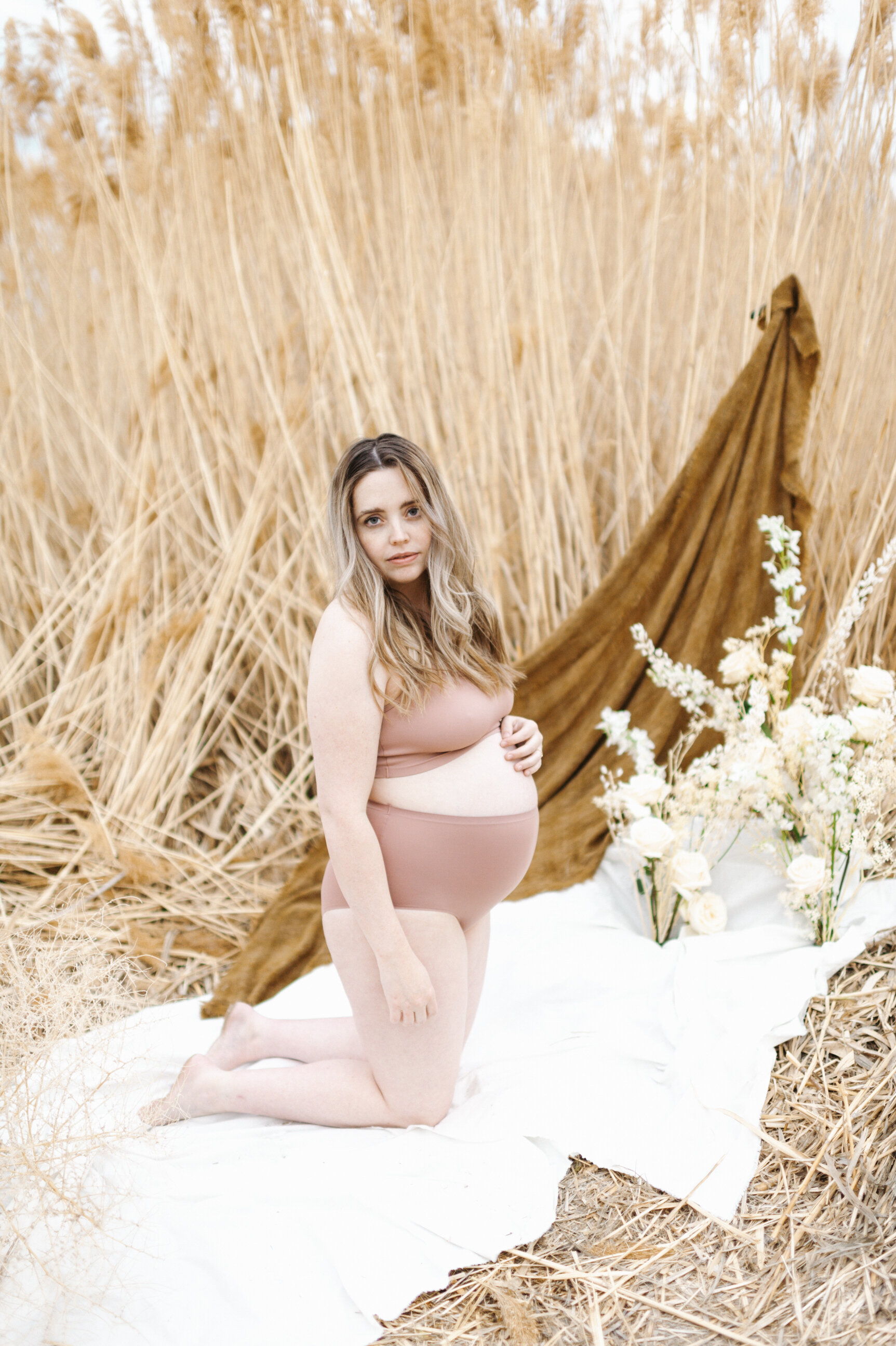 pregnant mom on white sheet in front of tall yellow grass