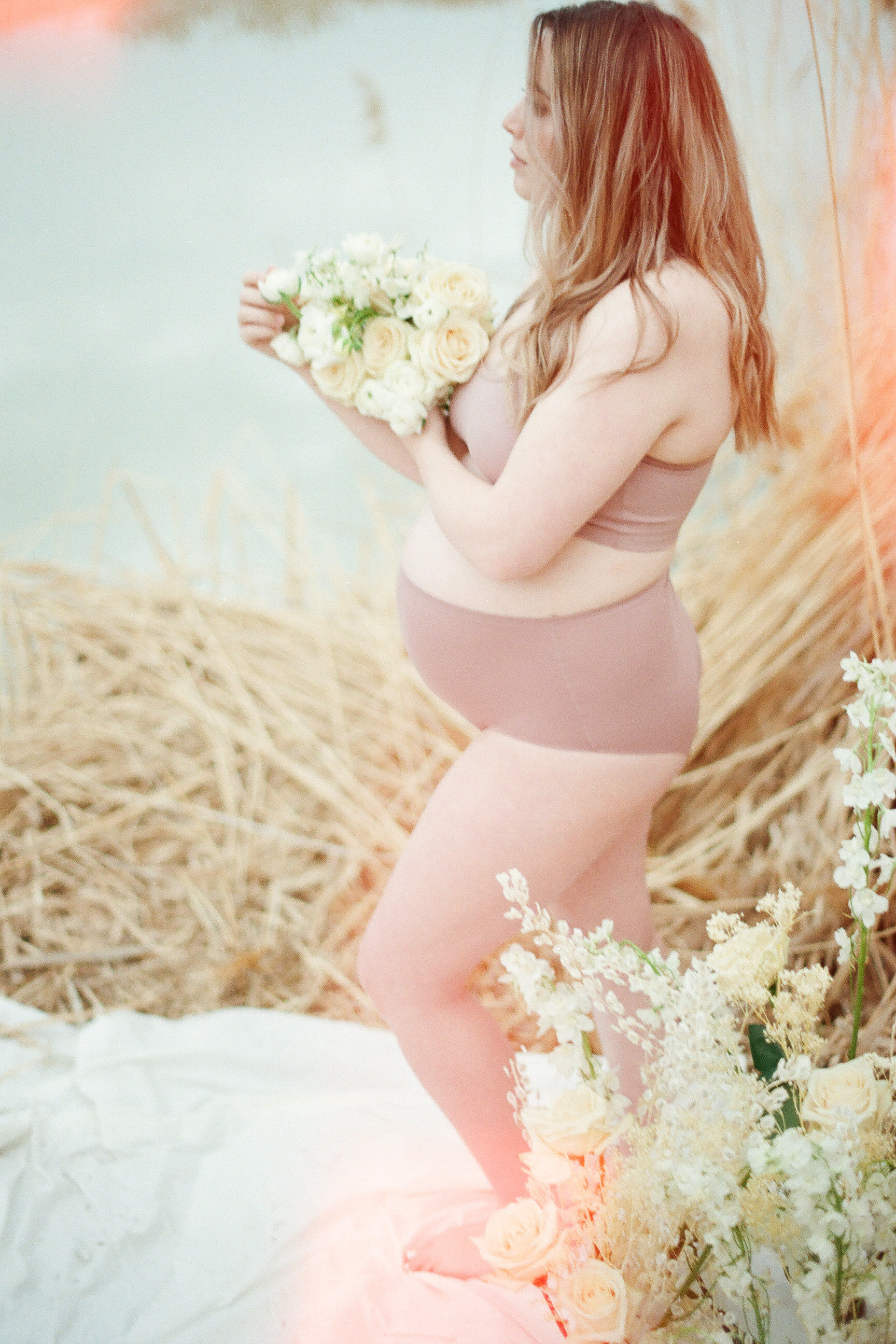 pregnant mom holding flowers bare belly in front of river