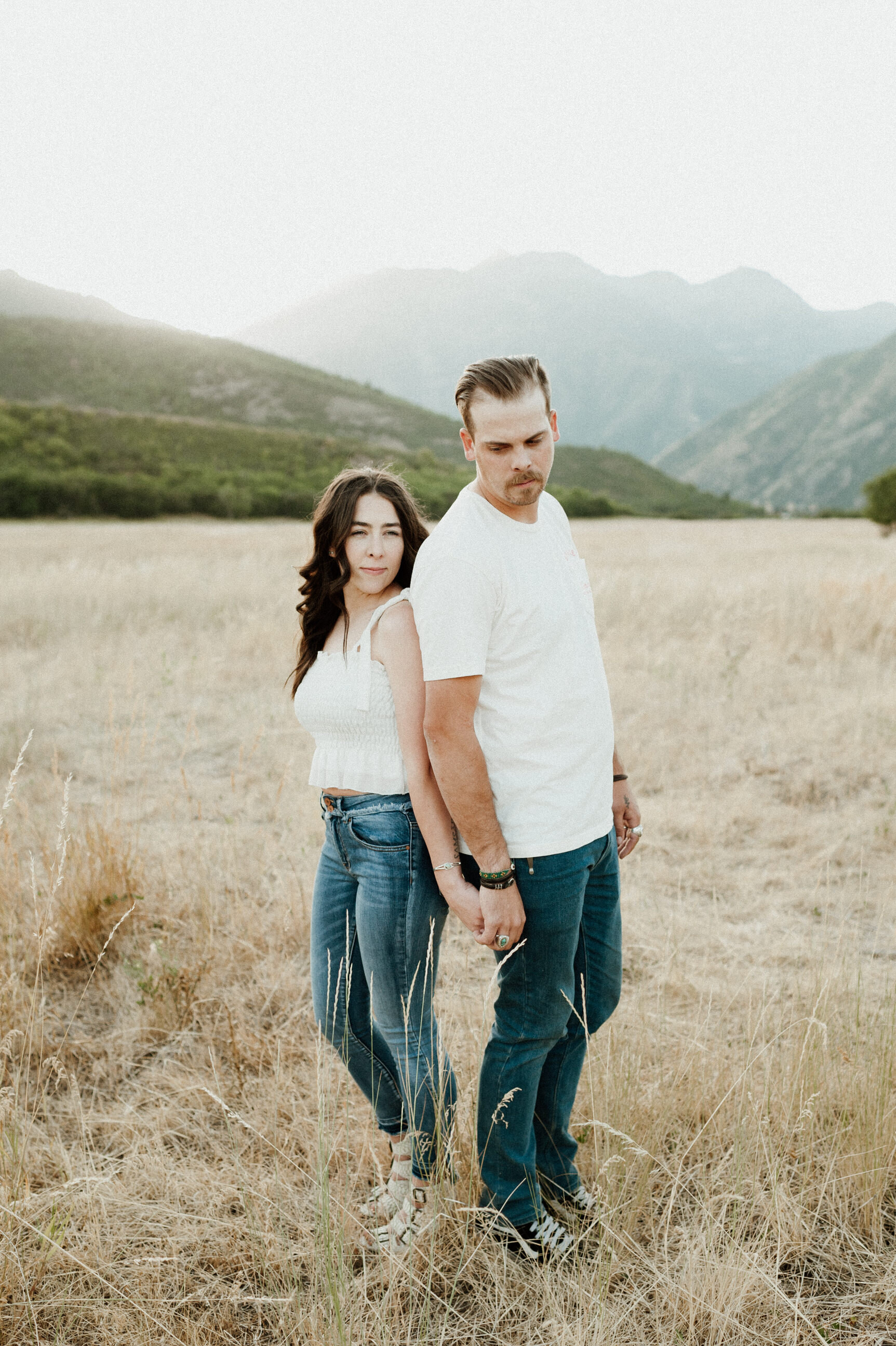 male female couple standing back to back in golden fields with mountains in background