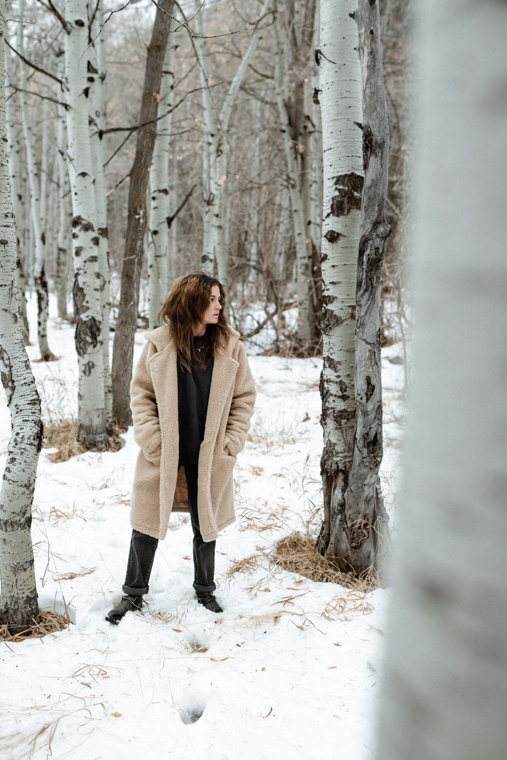 woman in fur coat standing in snow between quaky trees