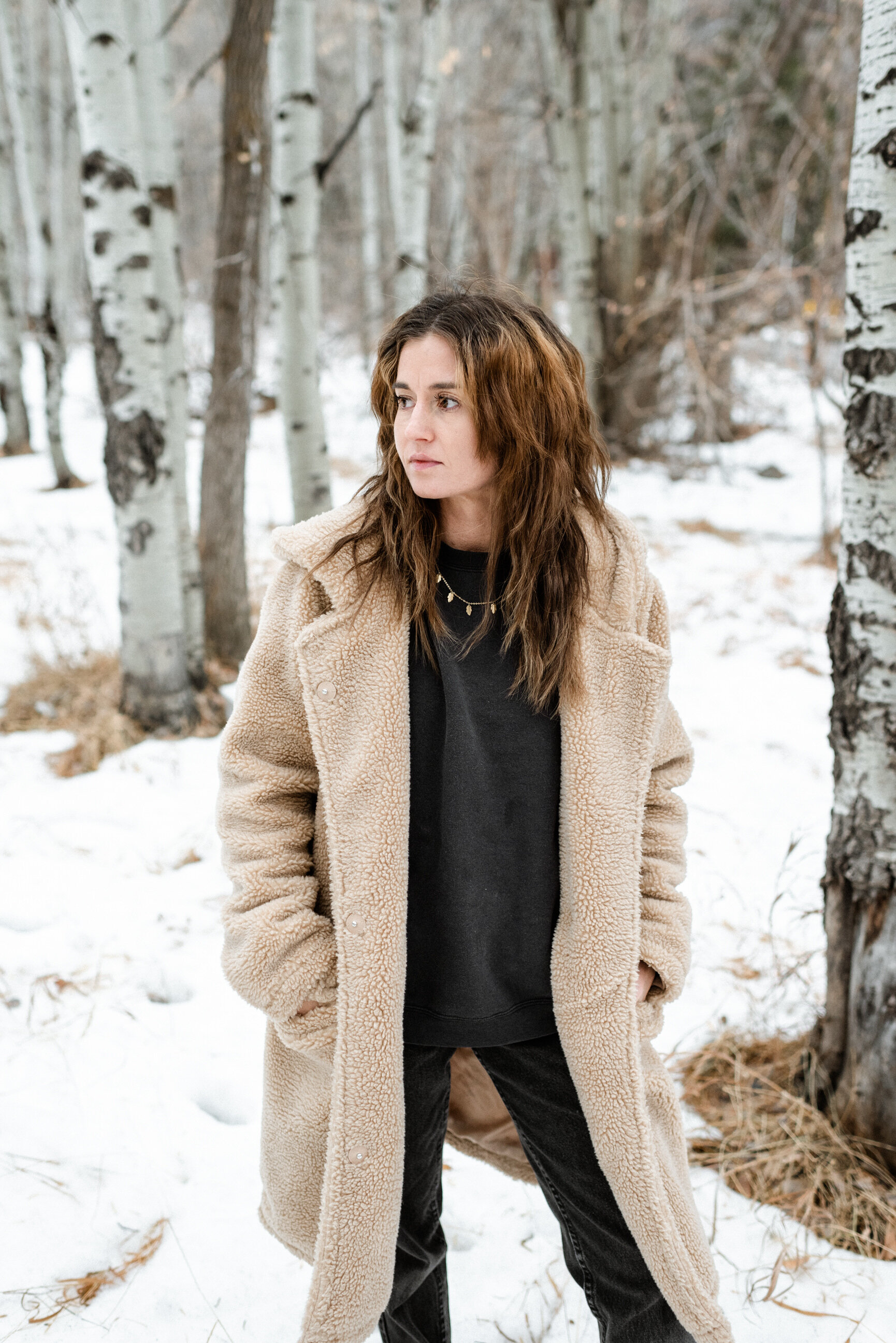 woman in fur coat standing in snow between quaky trees