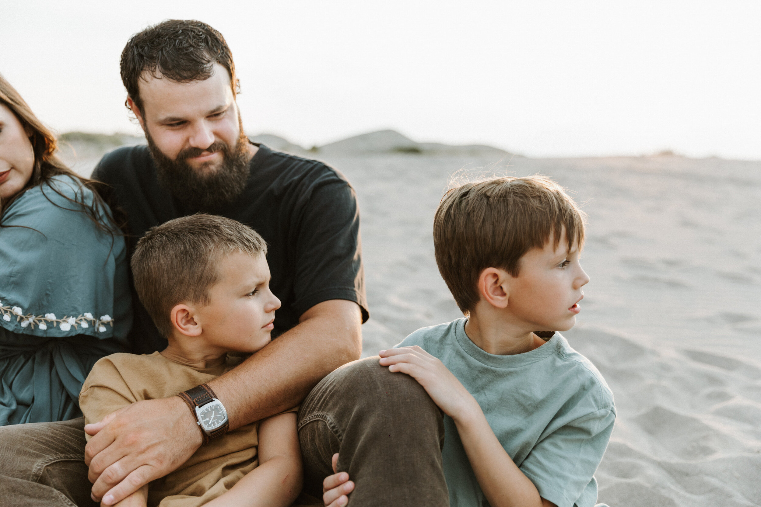profile of boys sitting by dad in sand
