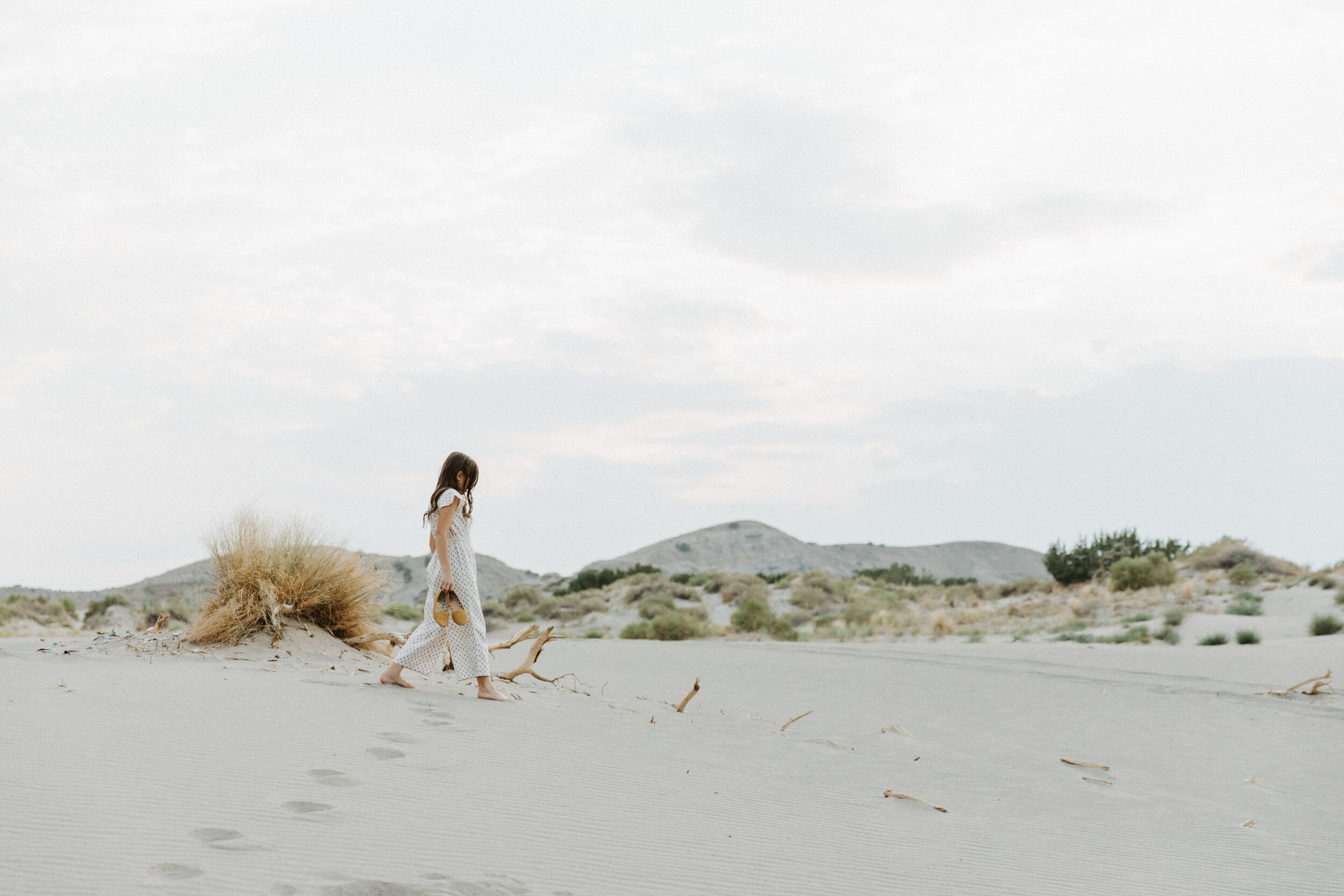 girl walking on sandy landscape holding shoes in hand