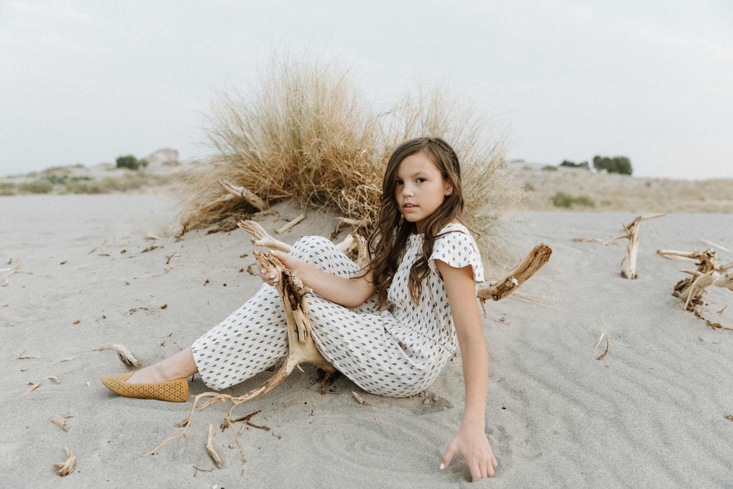 girl sitting on driftwood on sandy hillside