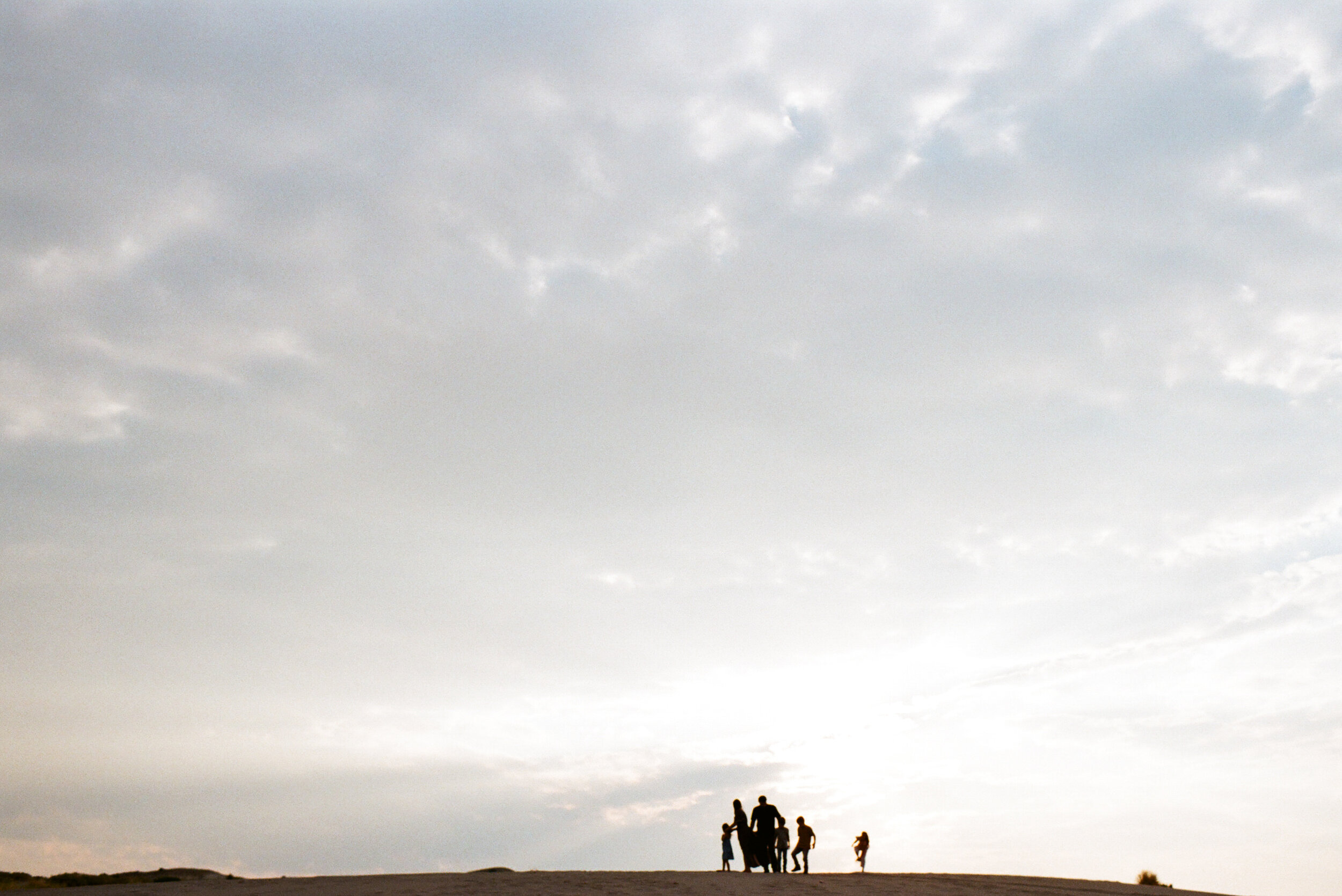 family standing on top of sand dune hill sillhoette