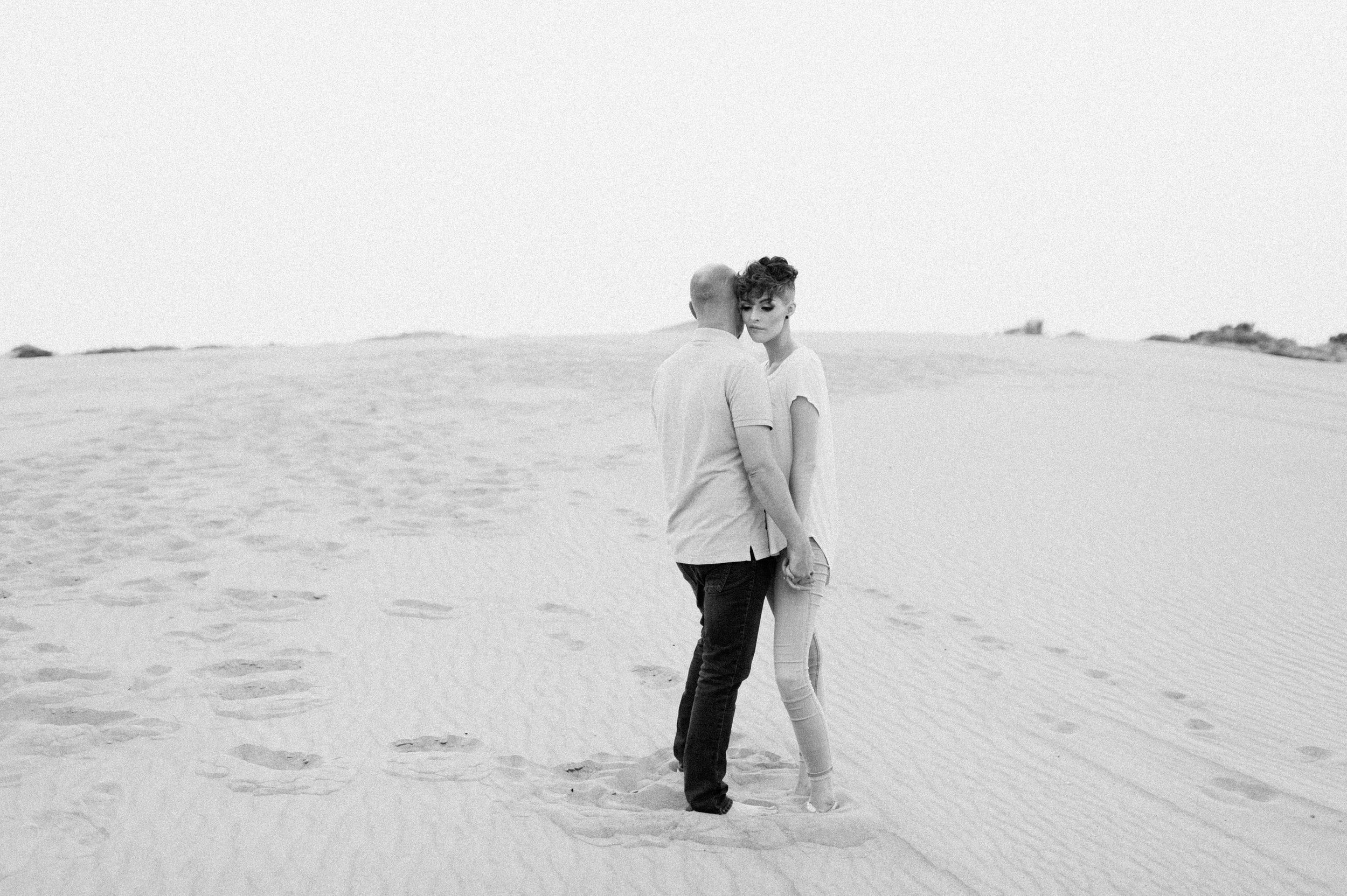 couple standing resting heads together at sand dunes