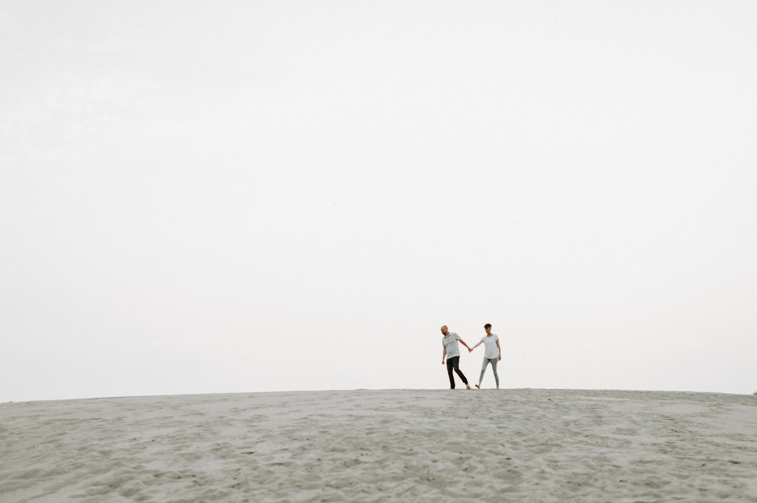 couple walking holding hands atop sand dune hill