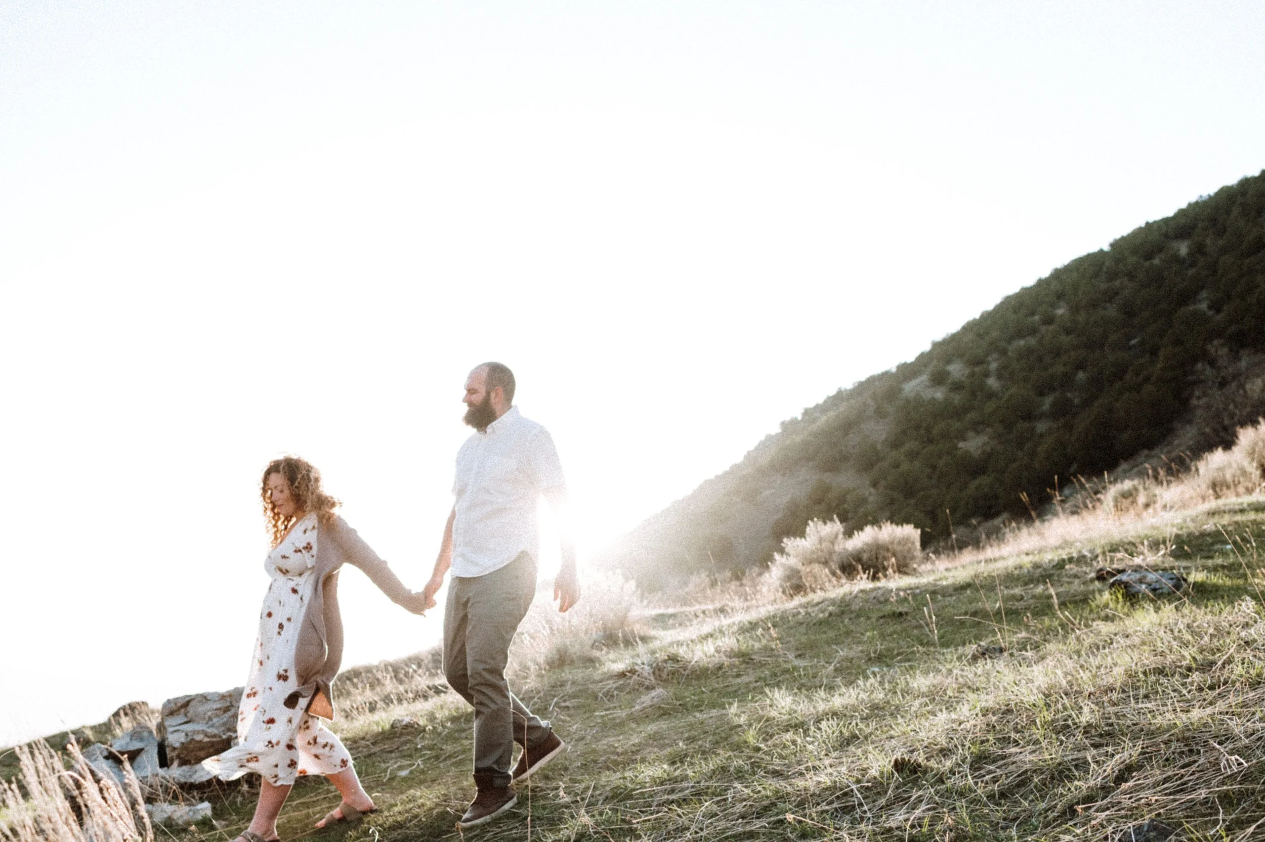 male female couple holding hands walking grassy hillside