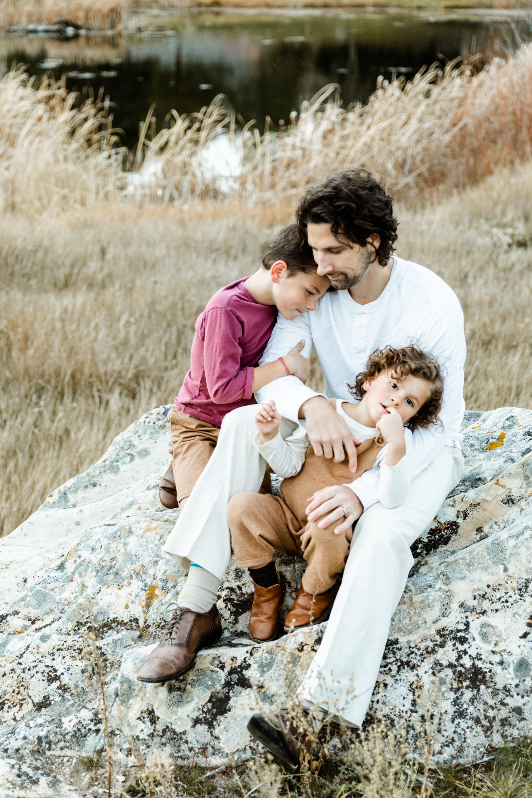 dad sitting on rock with son hugging shoulder other son on lap