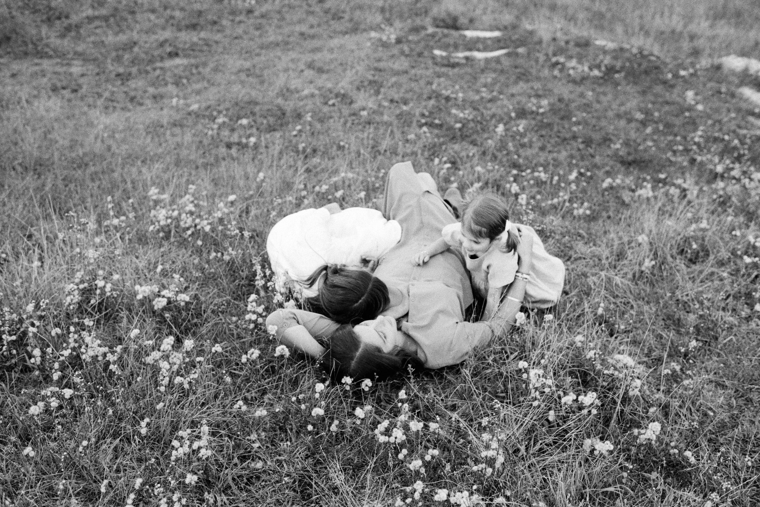 mom lying in grassy flower field with daughters lying on her