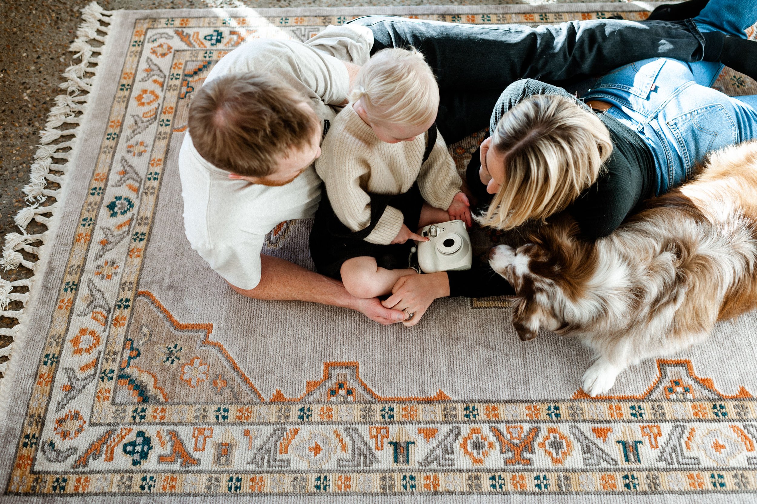 family lying on rug in rock entryway on neutral colored rug with dog