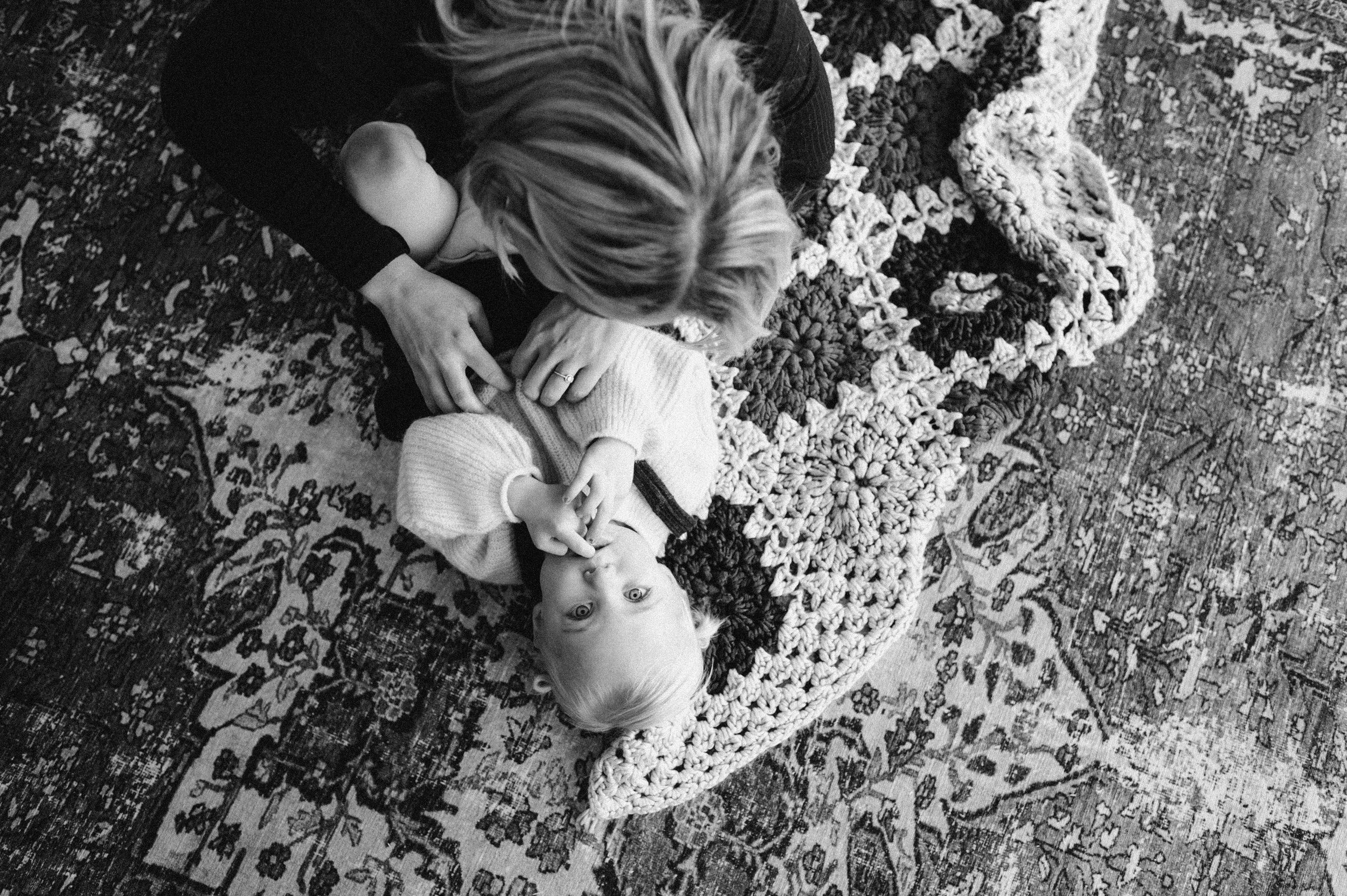 toddler lying on quilt and rug on floor mom brushing her cheek with finger