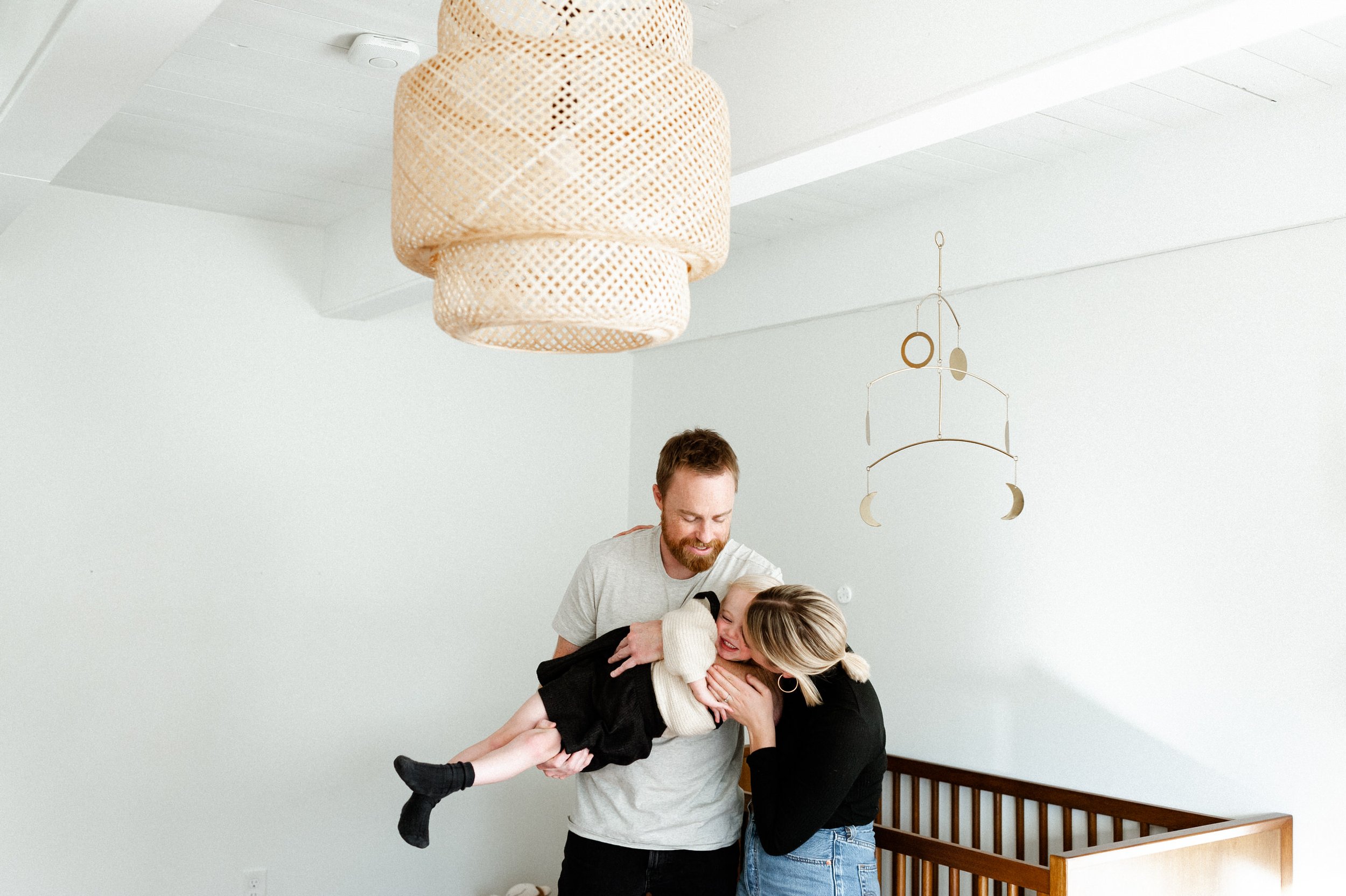 mom and dad holding toddler girl in nursery with wicker light and moon star mobile