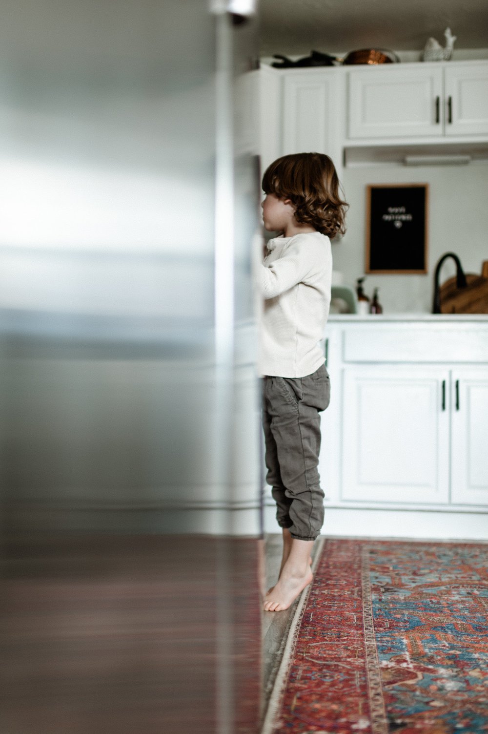 toddler boy on tiptoes reaching for something in kitchen cabinet