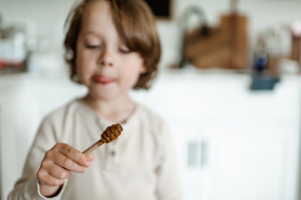 toddler boy in kitchen with honey on a honey dipper