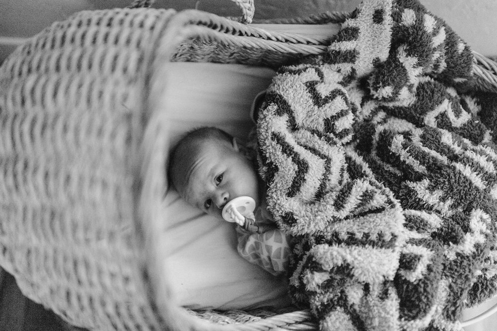 newborn baby lying in moses basket crib with thick aztec print blanket