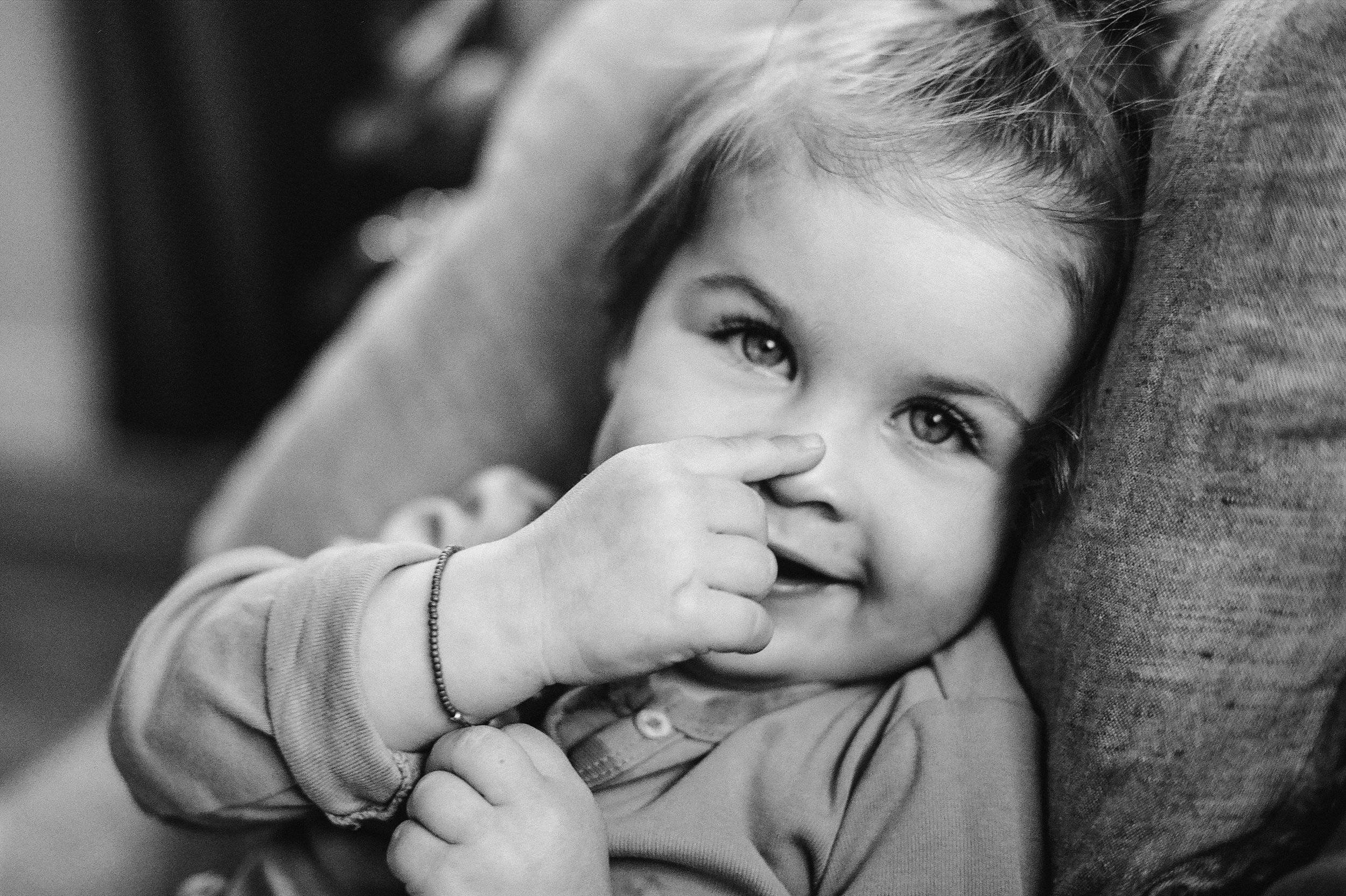 toddler girl touching nose looking at camera smiling black and white photo