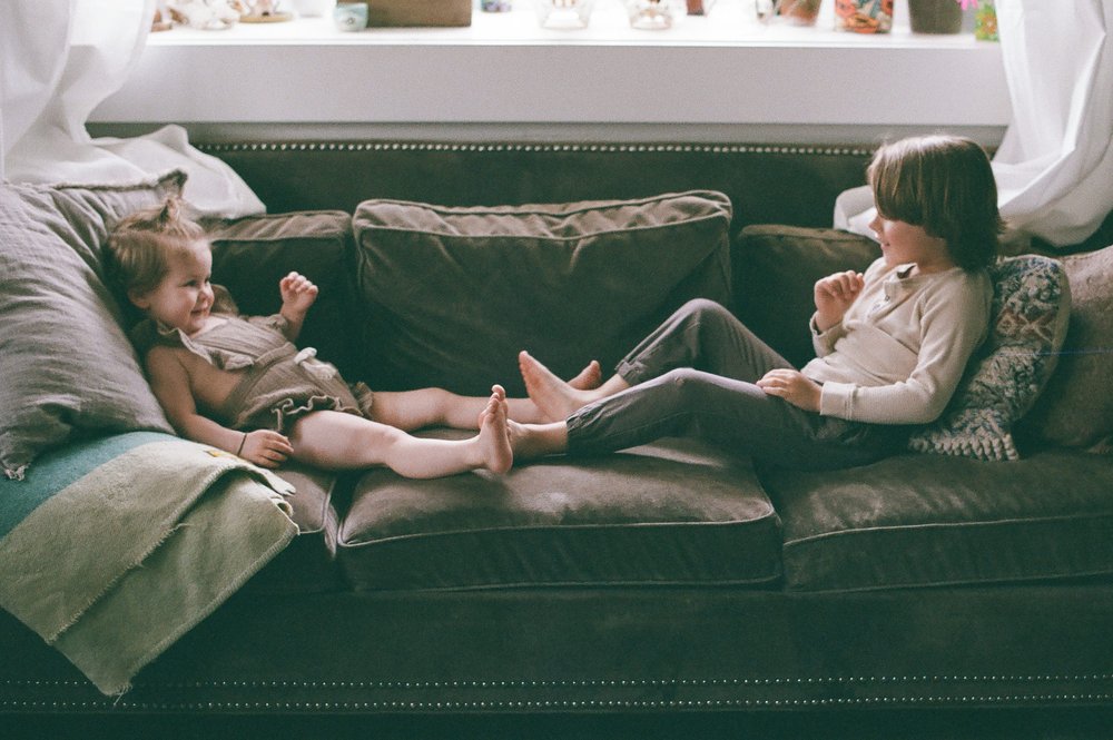 toddler boy and girl sitting on couch touching feet together