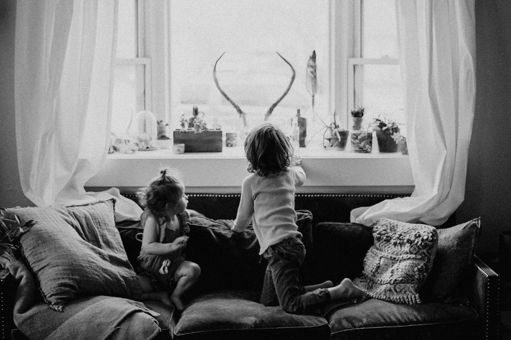 toddler boy and girl sitting on couch looking out window