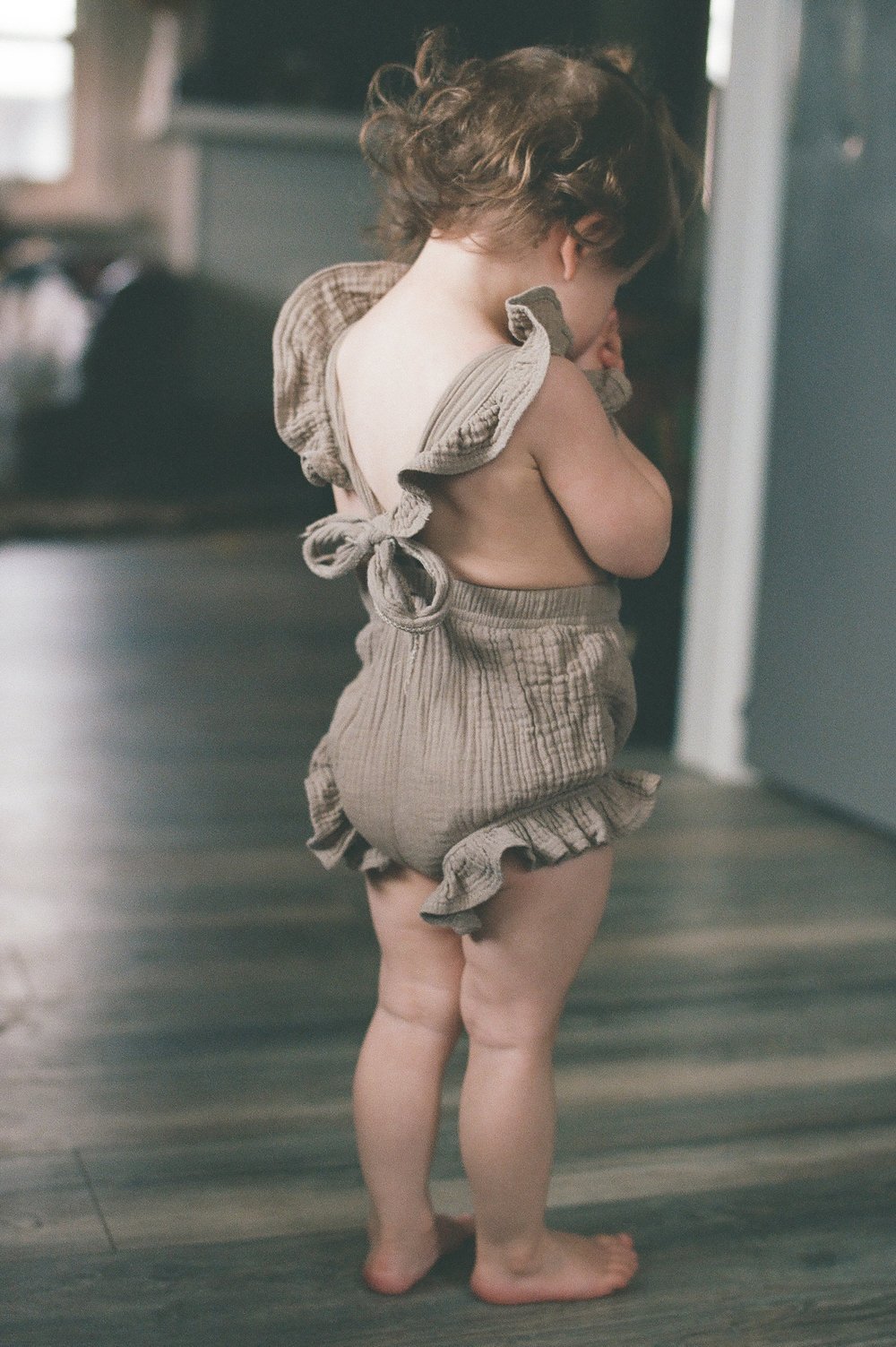 toddler girl standing on wooden floor in light brown romper