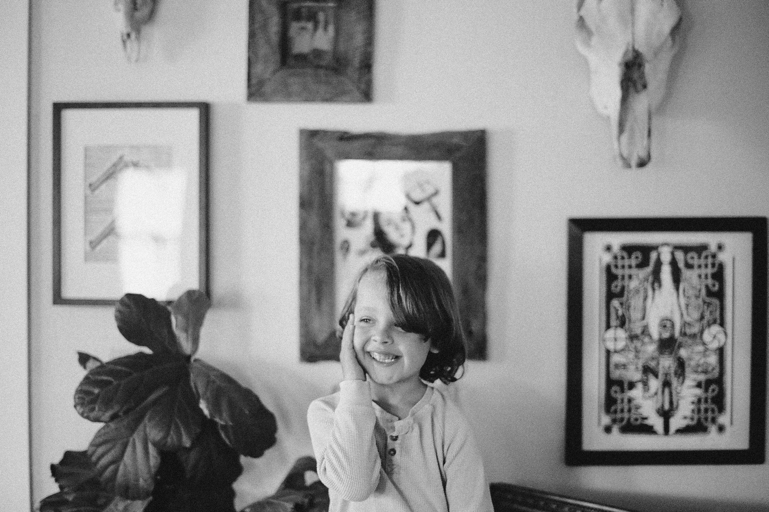 toddler boy laughing standing in front of photo frame gallery wall