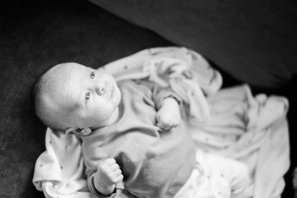 black and white film photo newborn baby lying on swaddle blanket looking up at window