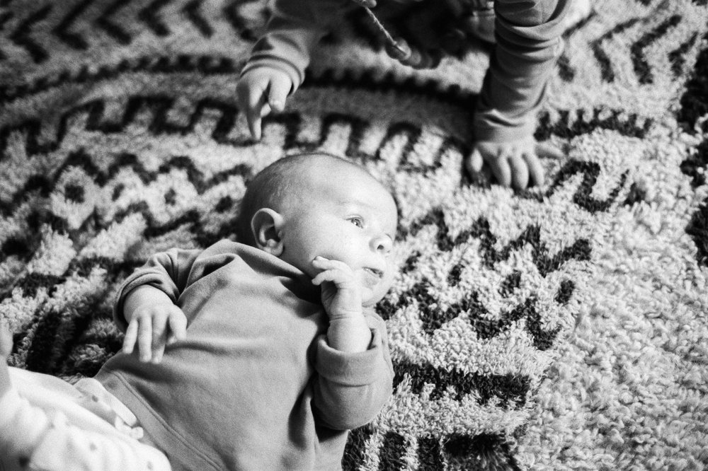 toddler girl pointing at baby brother lying on aztec pattern blanket black and white