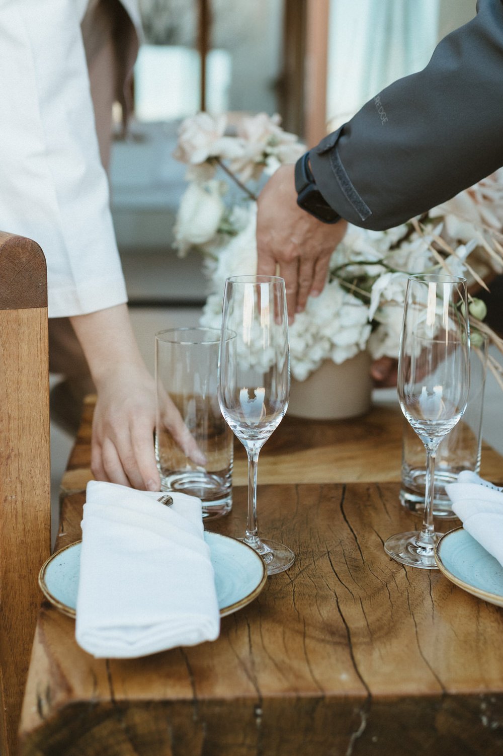 hands setting wine glasses onto wooden table with florals and charcuterie board