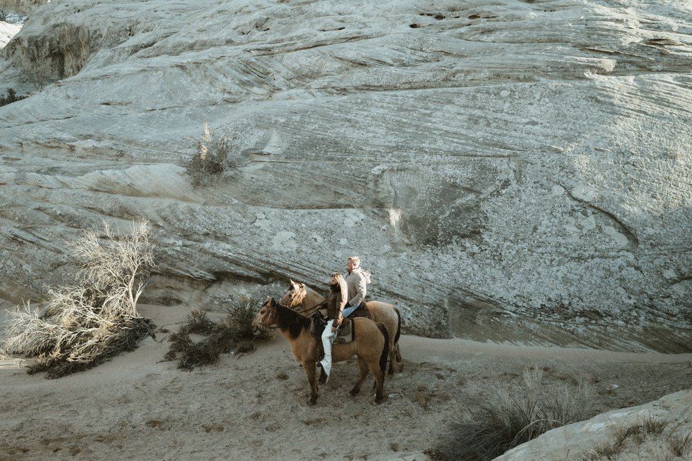 couple on brown horses riding on sand through white rock canyon at amangiri