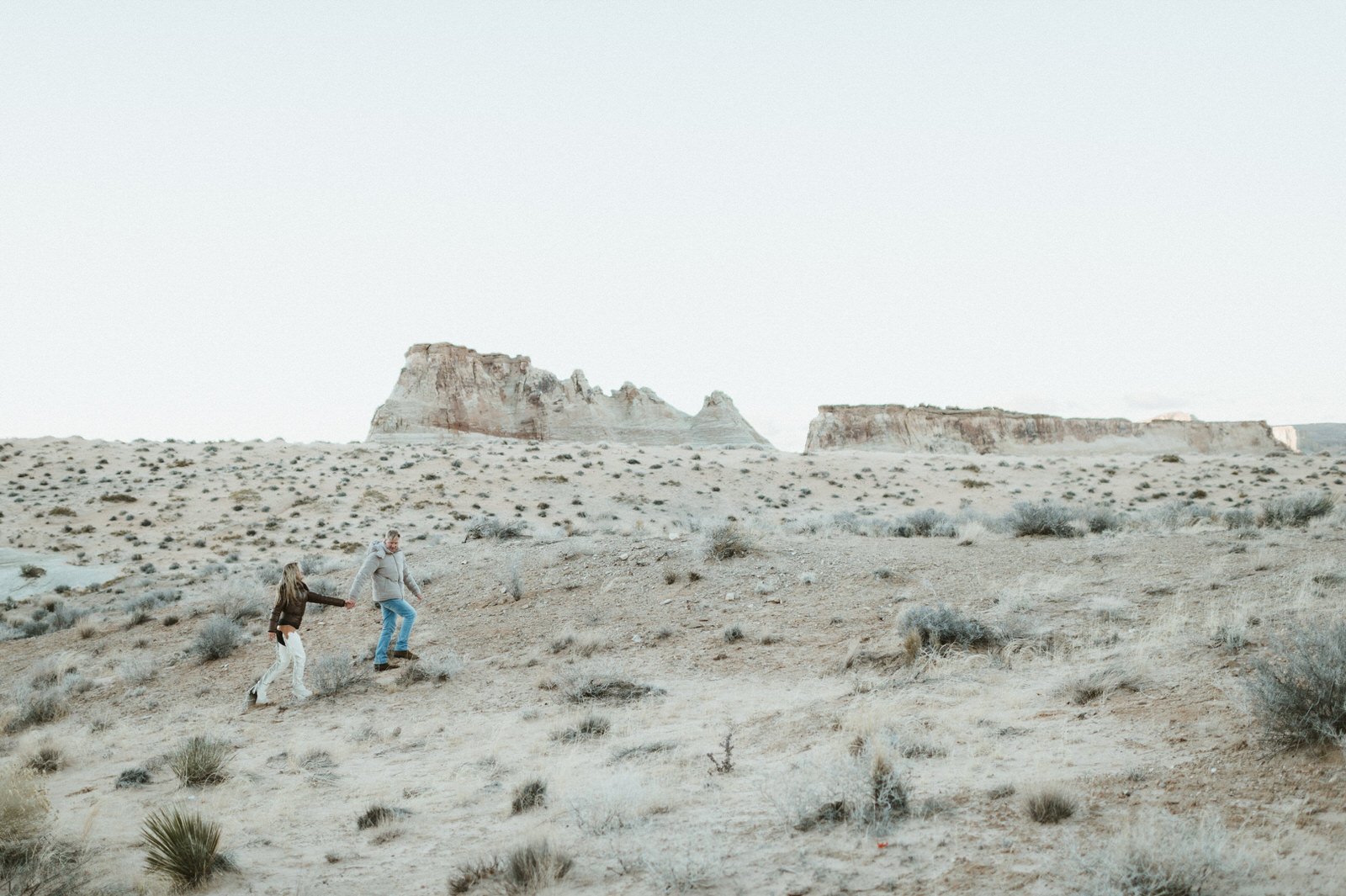 man and woman couple holding hands walking through desert landscape with mesa background amangiri resort