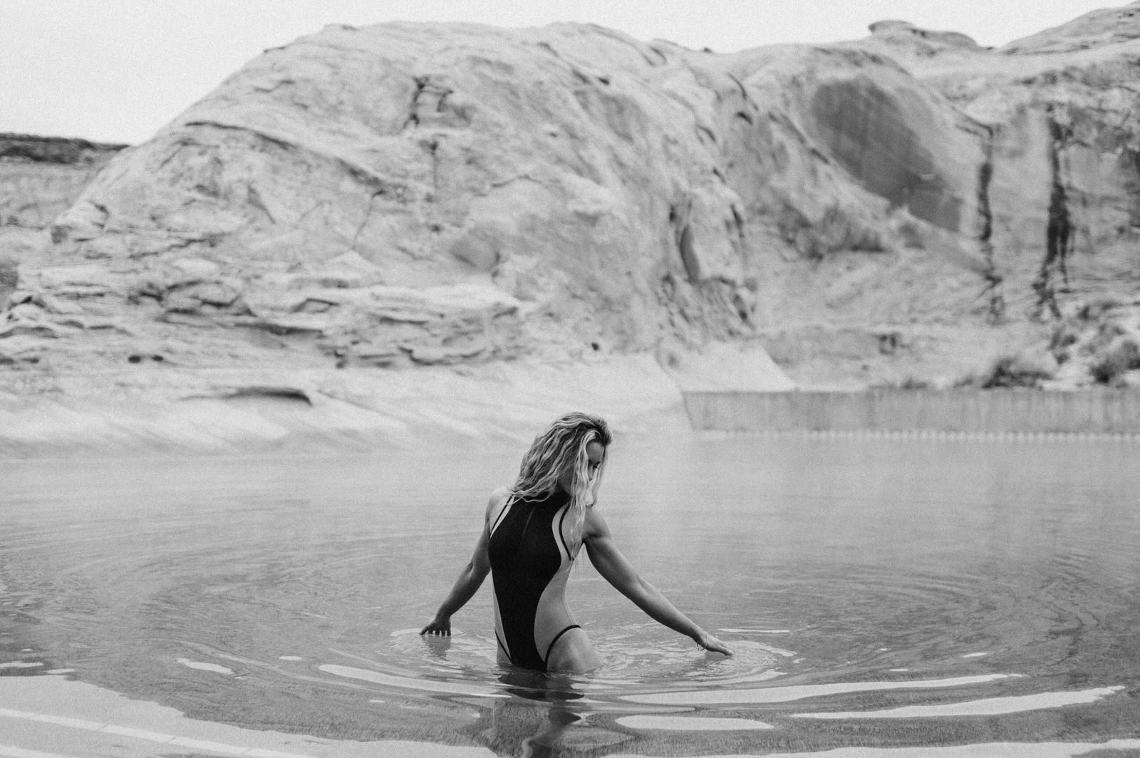 black and white photo woman in black swimsuit making small ripples in water with fingertips touching water amangiri pool