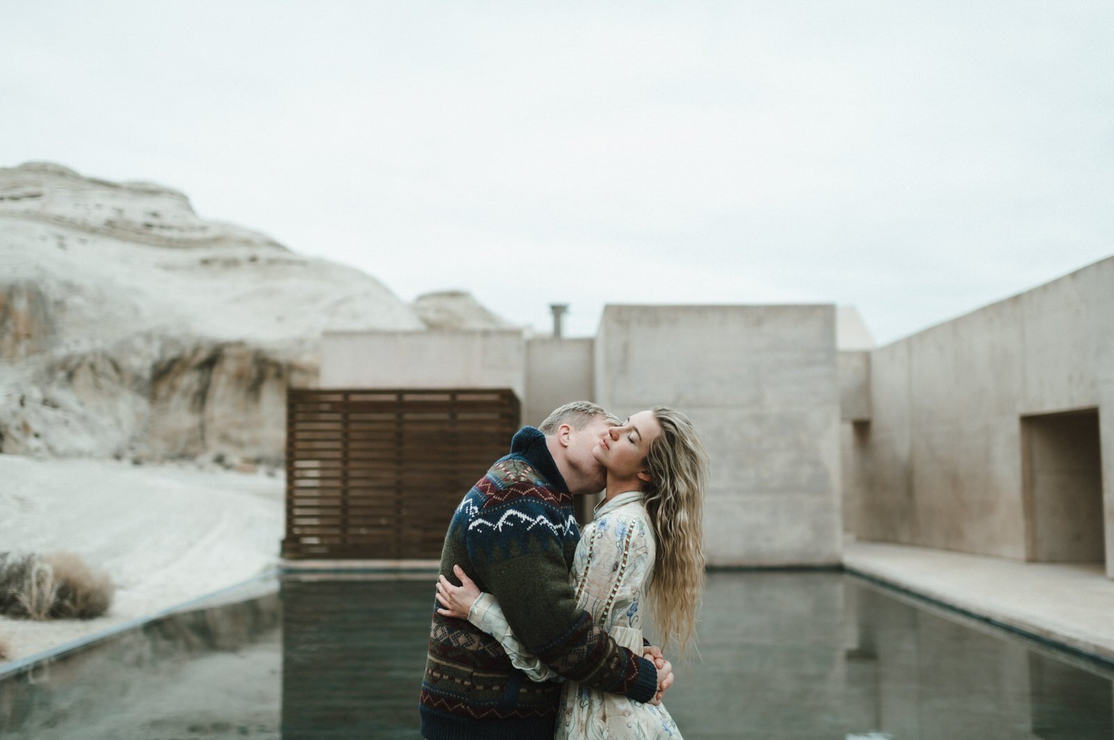 man kneeling down proposing to woman on concrete wall with desert landscape and mesas in the background amangiri