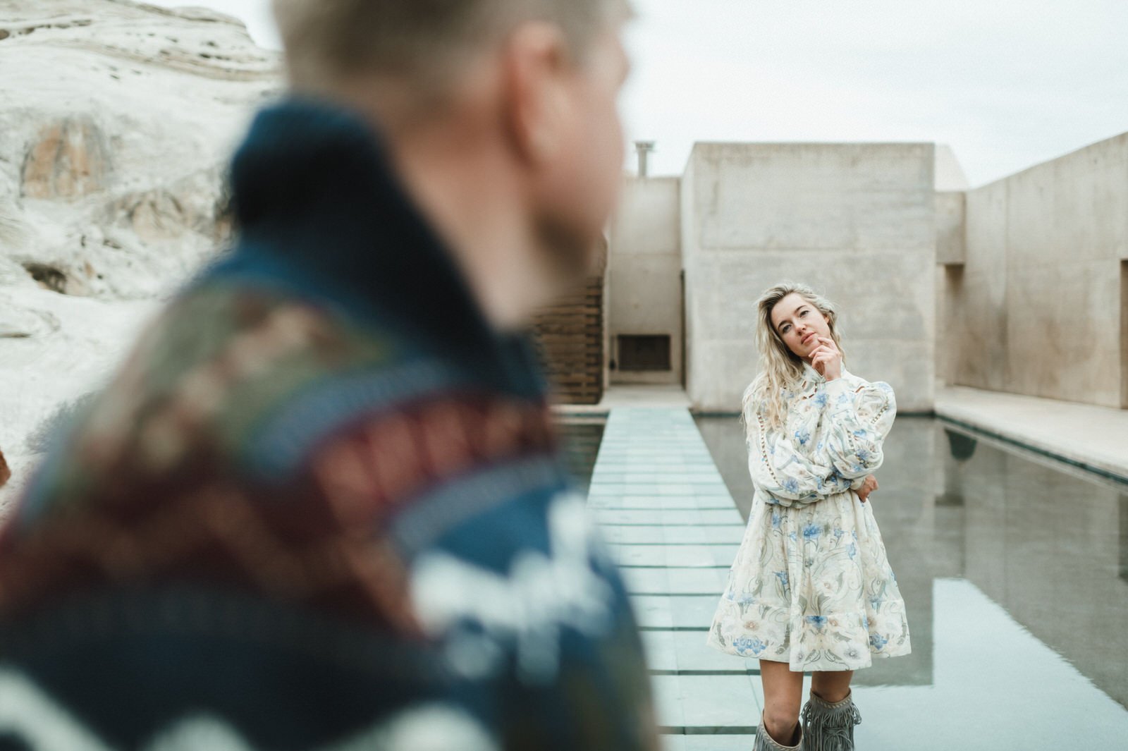 woman standing on blue steps across pool concrete wall background man blurry in foreground looking back at her