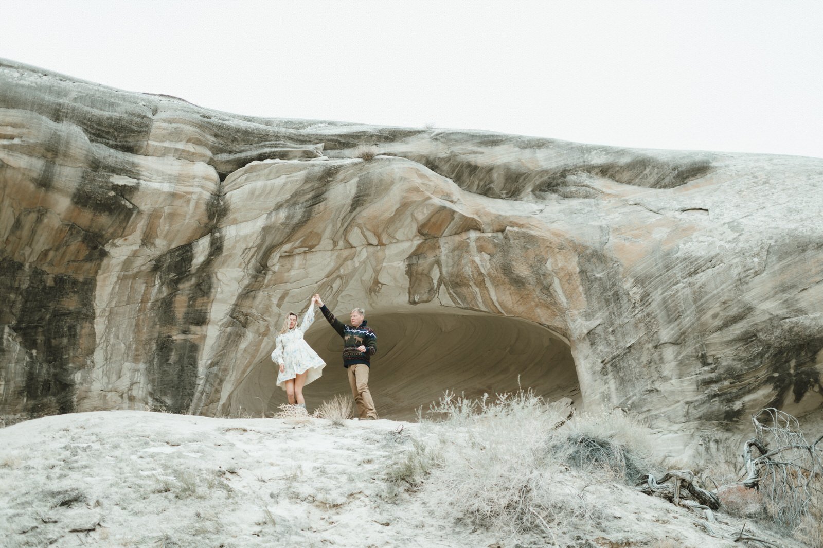 man and woman in front of desert stone face man twirling woman in dress