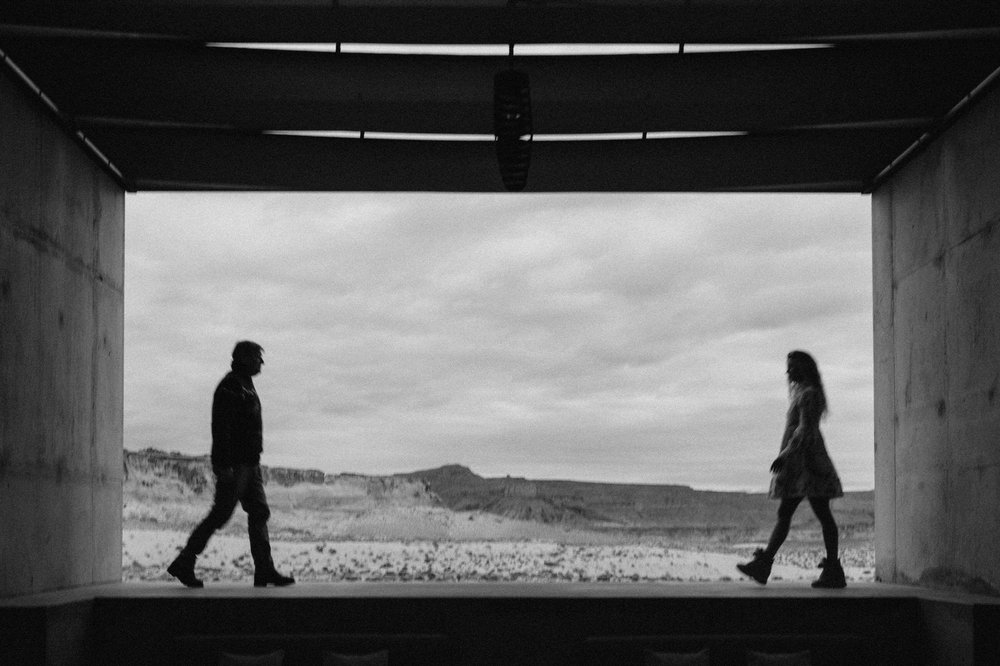 black and white photo man and woman walking toward each other with desert framed by concrete walls in background amangiri