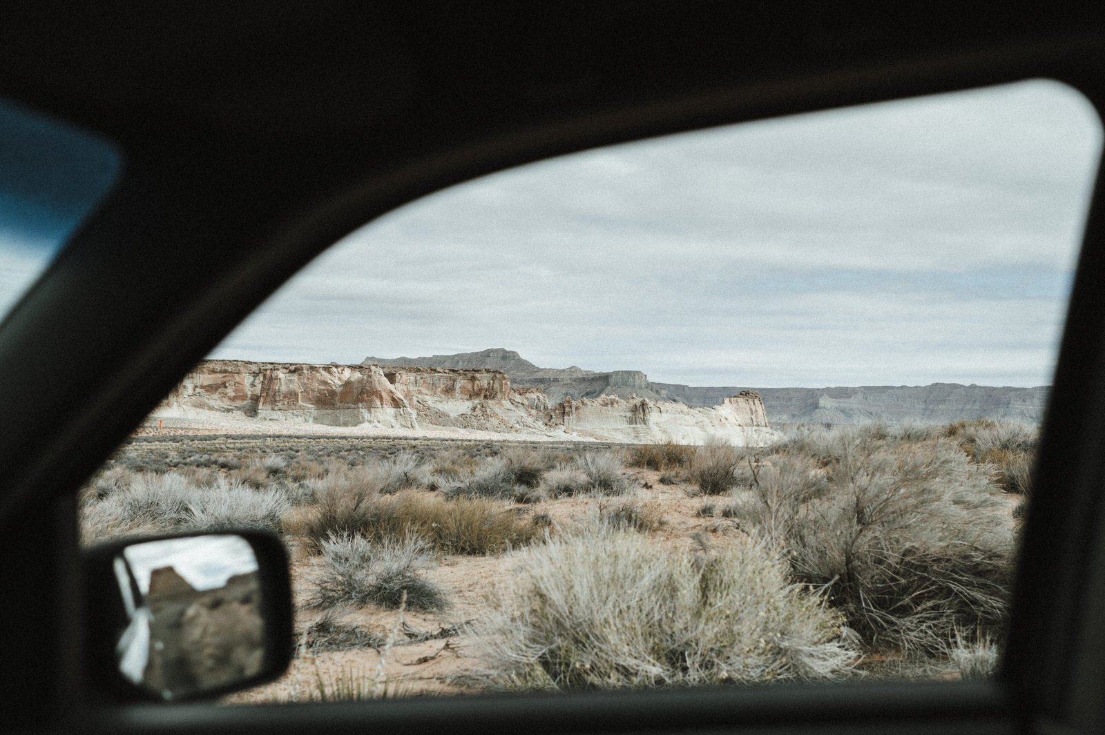 view through car window framing desert with reflection of mesas in mirror amangiri