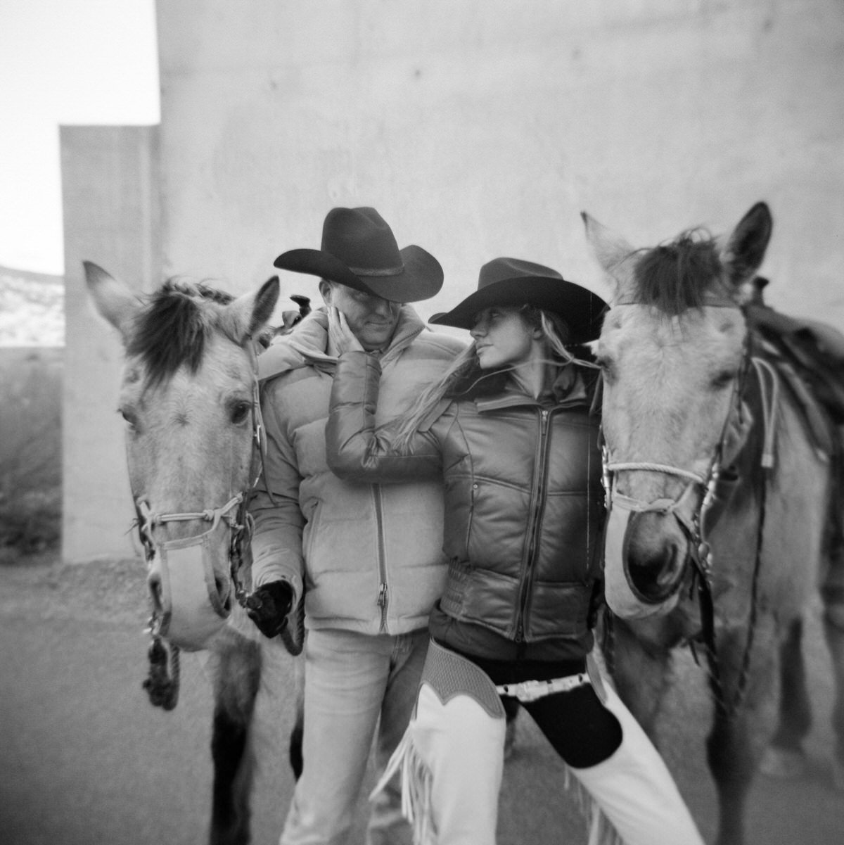 black and white film of couple wearing cowboy hats standing next to horses at amangiri